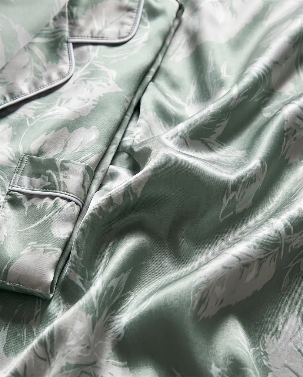 sage-satin-pajama-fabric-texture-detail لقطة مقربة لخامة بيجامة ساتان حرير خضراء ولمعتها الفاخرة وتفاصيل الجيب